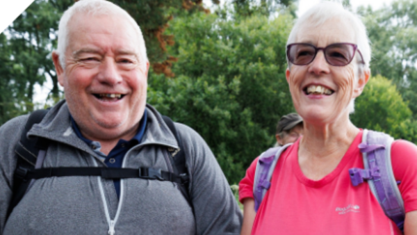 A man and a woman smiling to camera during a walk on a sunny day